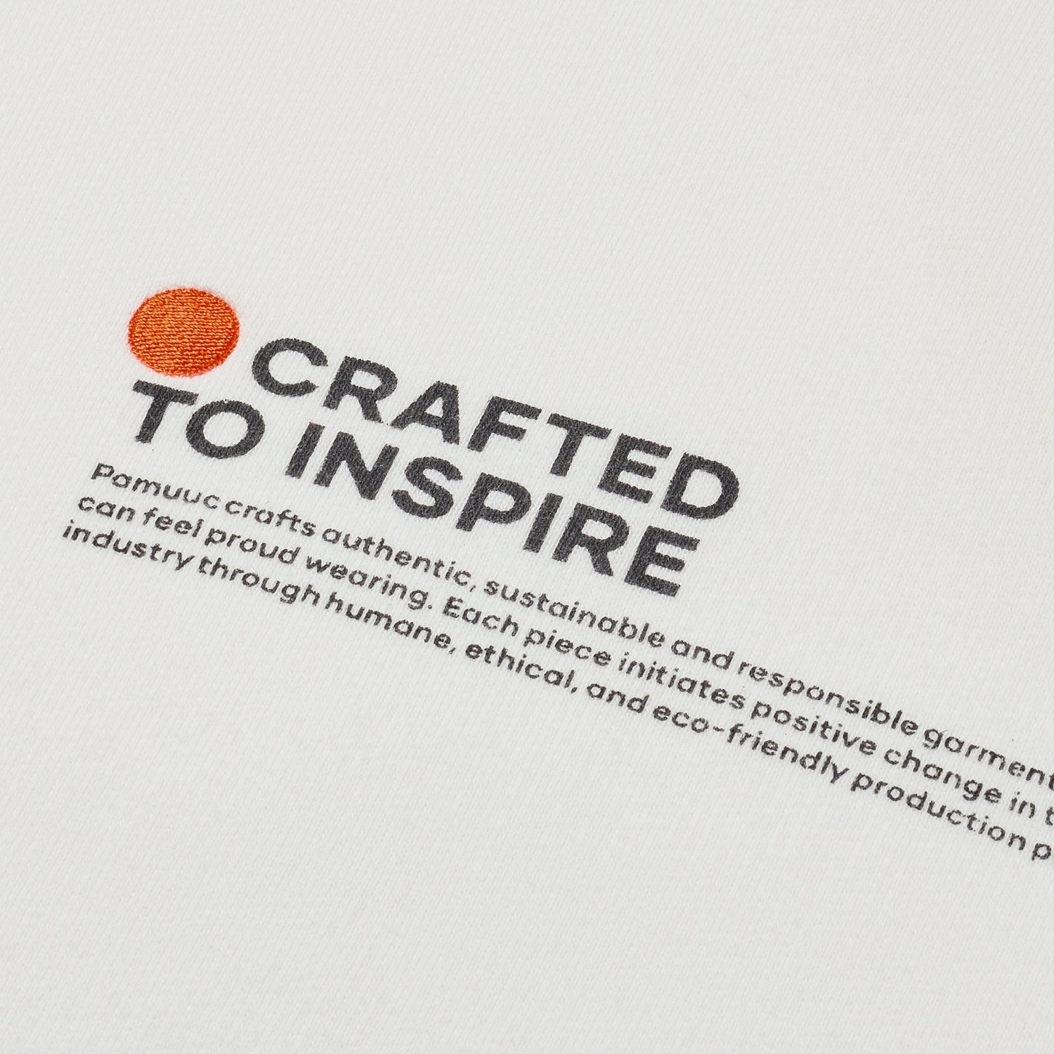 Close-up of white sweatshirt's fabric with "Crafted to Inspire" print and Pamuuc logo.