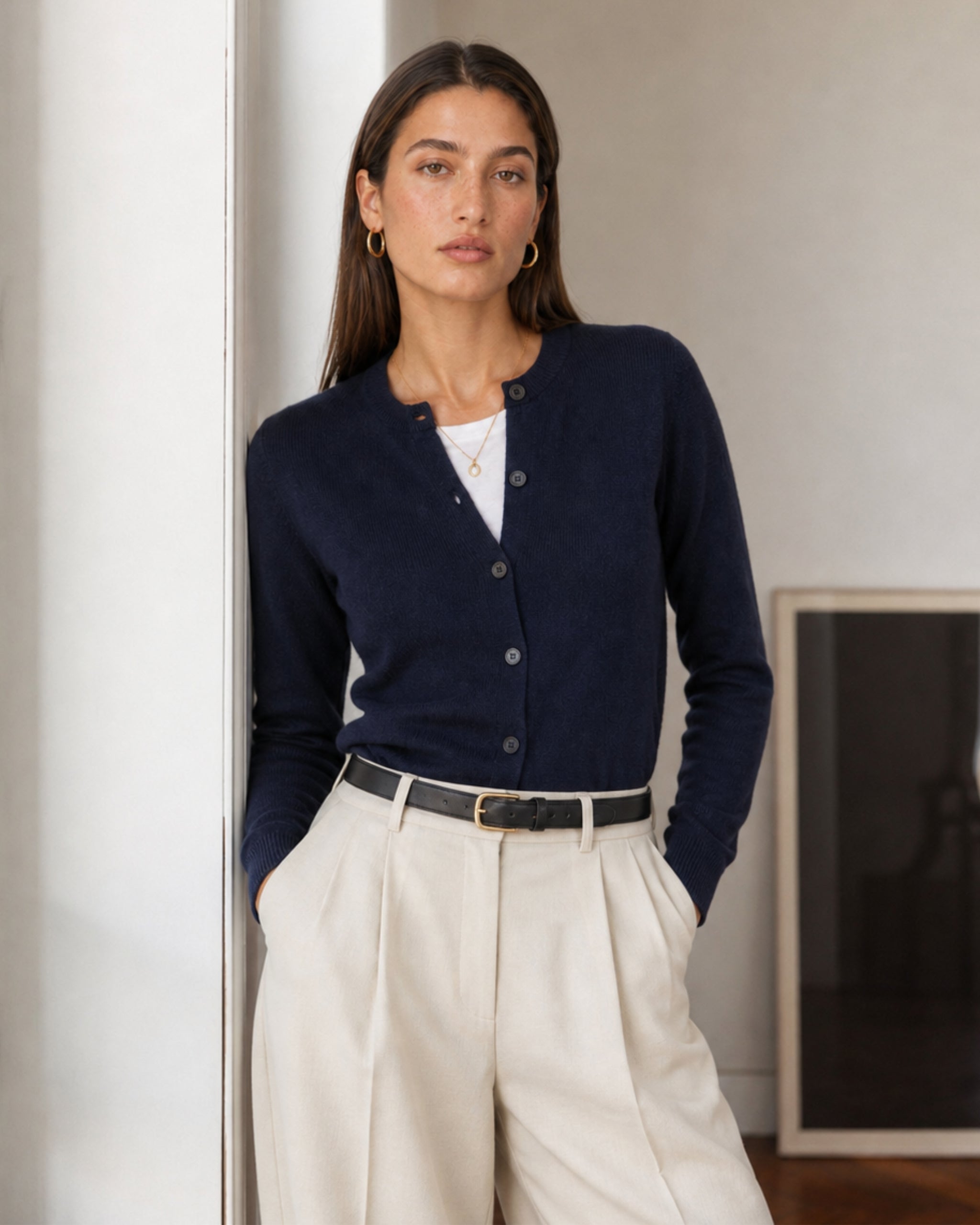 Frau mit Merino-Cardigan in Marineblau und cream mit Bundfalten Hose im Innenraum