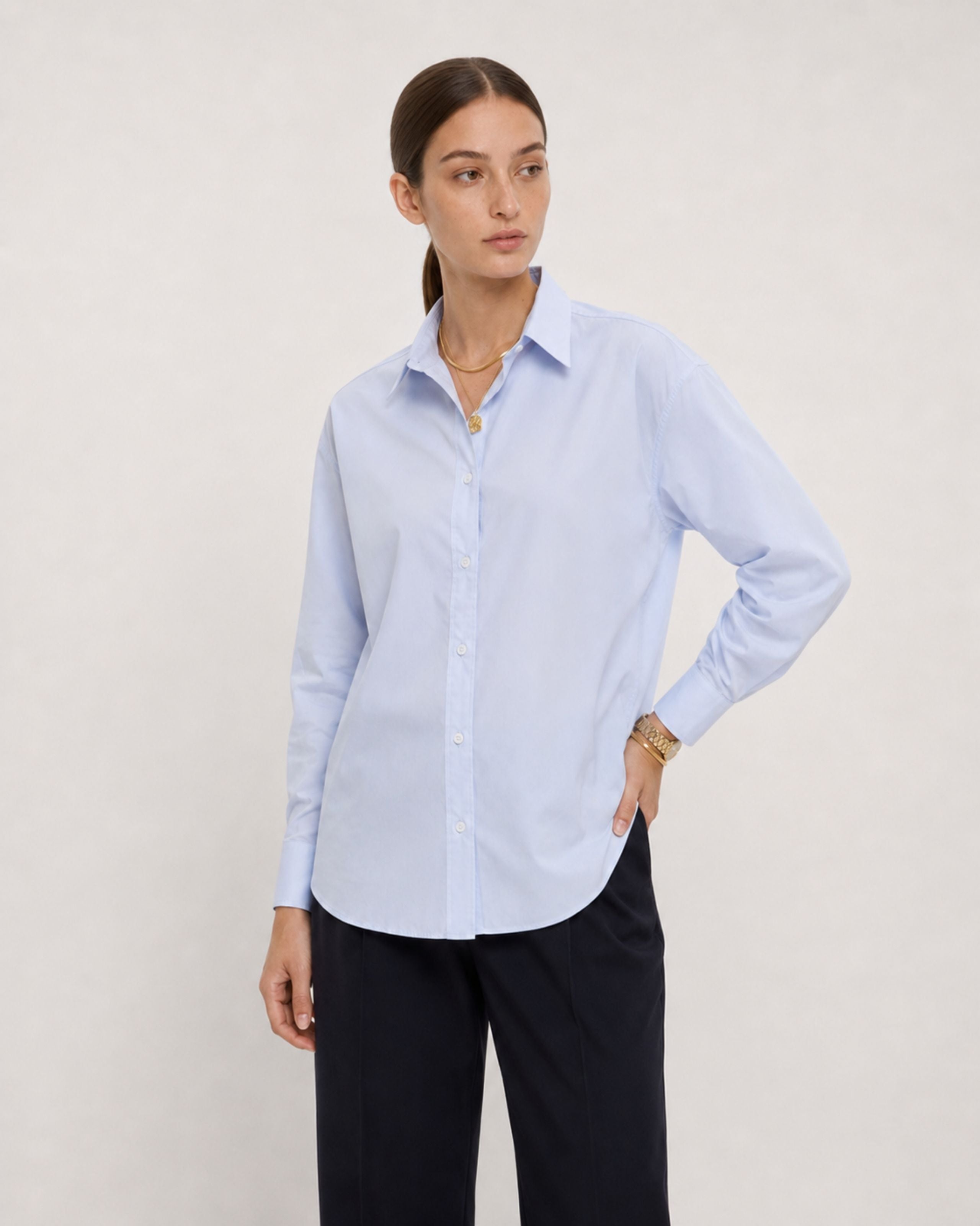 Model in a light blue striped shirt and navy trousers, hand on hip