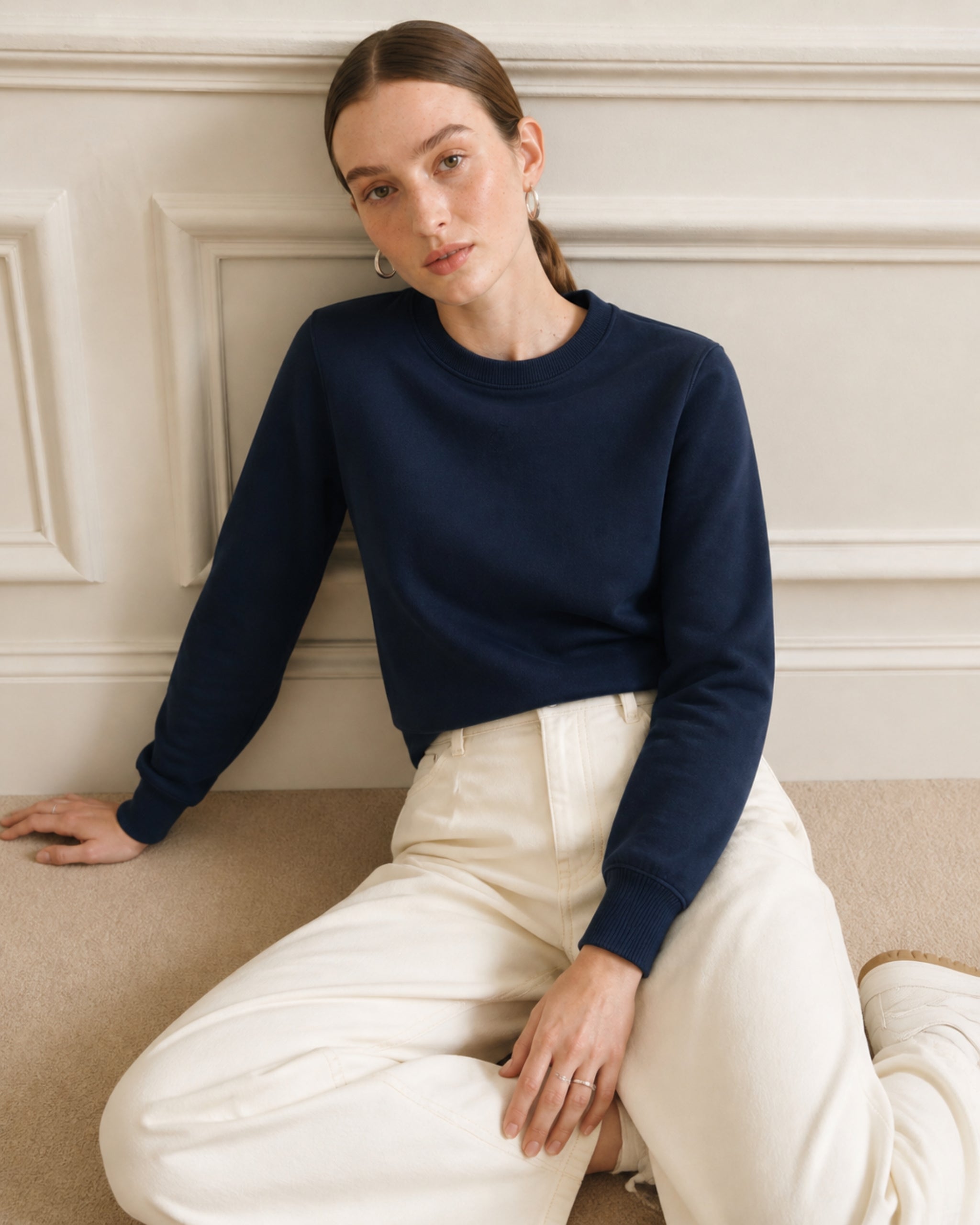 Frau mit Baumwoll-Sweatshirt in Marineblau und Hose in Creme sitzend auf sofa